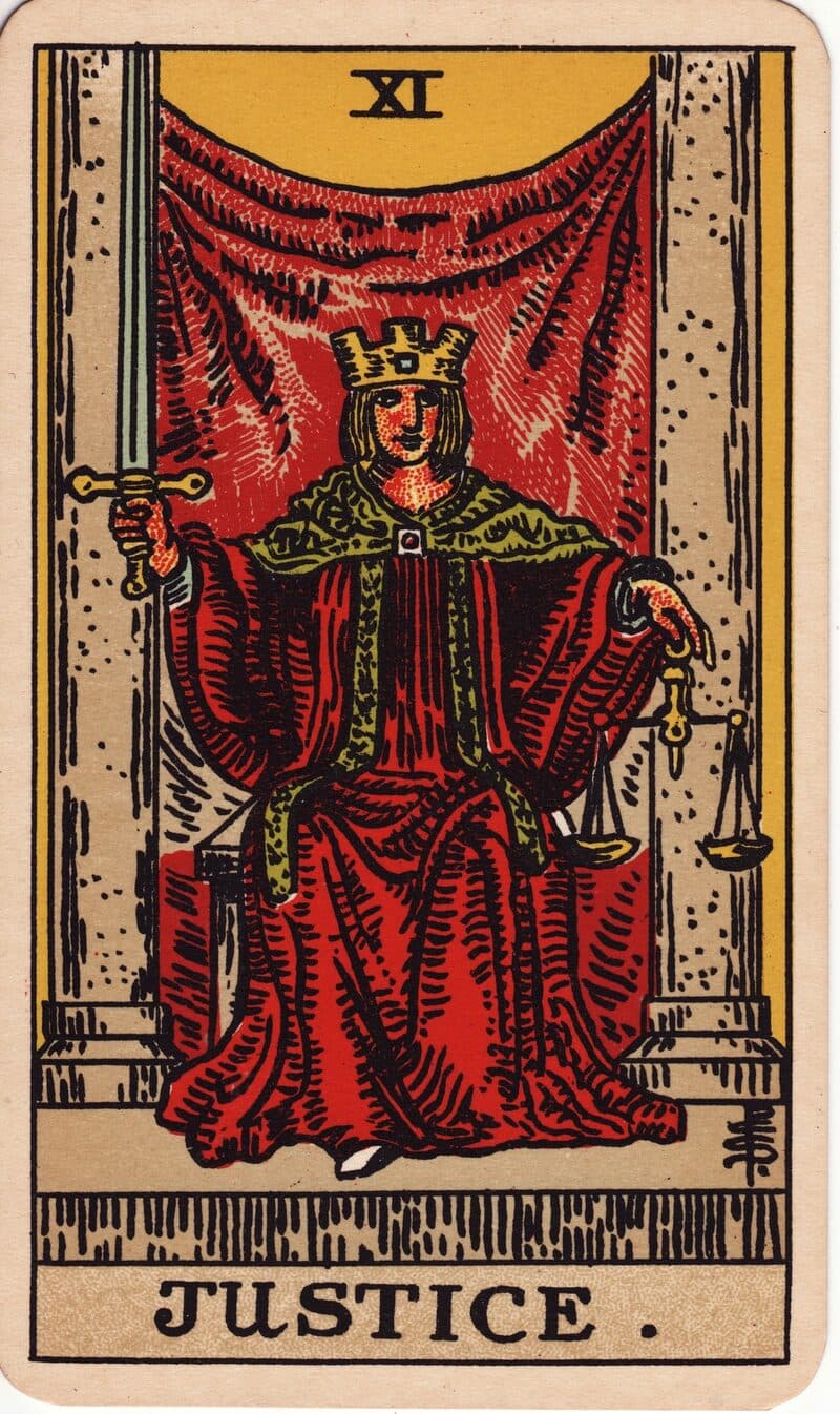 Justice tarot card — crowned figure holding a raised sword and balanced scales between two pillars, Rider-Waite-Smith deck