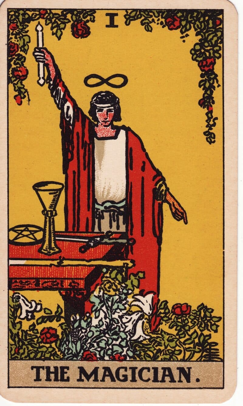 The Magician tarot card — robed figure at altar with all four suit emblems, one hand raised skyward, Rider-Waite-Smith deck
