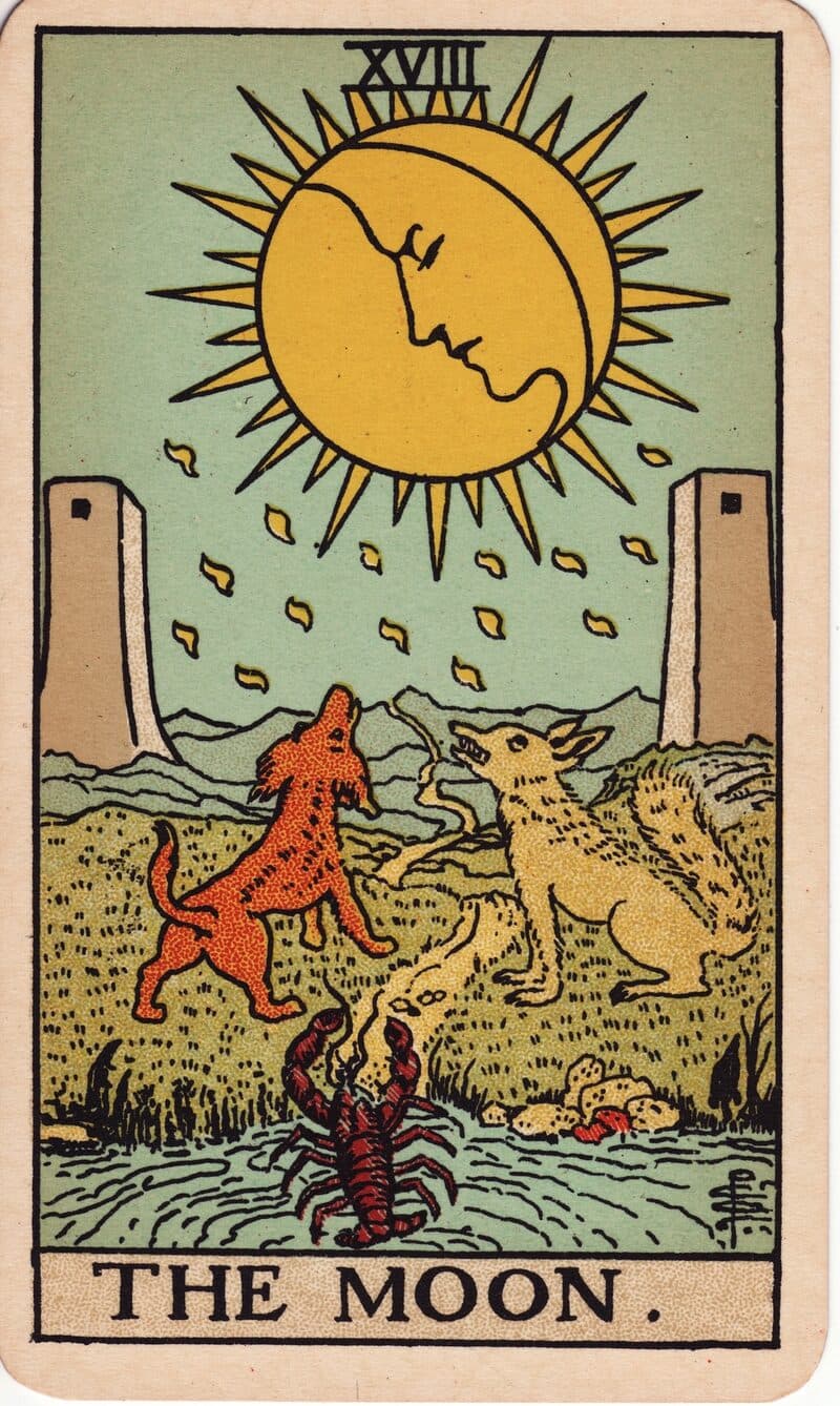 The Moon tarot card — moon face above a winding path with howling wolf, dog, and crayfish emerging from water, Rider-Waite-Smith deck